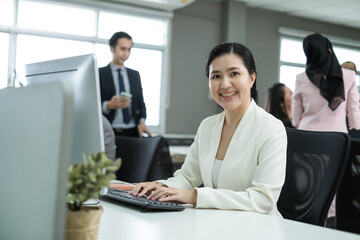 Fototapeta premium Confident middle aged business Asian woman sitting at her workplace in office. Portrait Asian female worker in office.