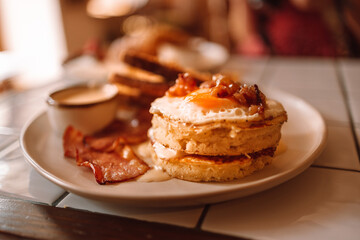 English breakfast with bacon, sausage, fried egg on a white plate on wooden background in a cafe on a summer morning