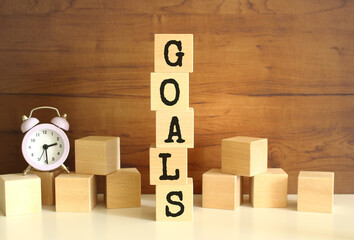 Five wooden cubes stacked vertically to form the word GOALS on a brown background.