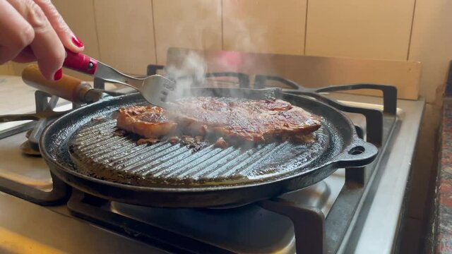 A Rib Steak in a Cast-iron Pan, Woman prodding the Meat with a Fork. Close Up. 4K Resolution.