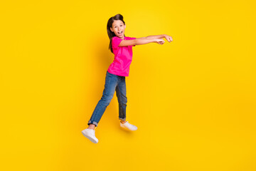 Fototapeta na wymiar Photo of positive little cowgirl jump pretend ride horse wear pink t-shirt jeans shoes isolated yellow color background