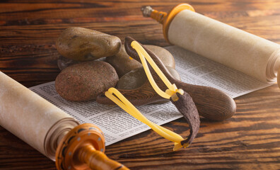 Five Smooth Stones and Sling Shot on a Hebrew Scroll Symbolising the Story of David and Goliath .