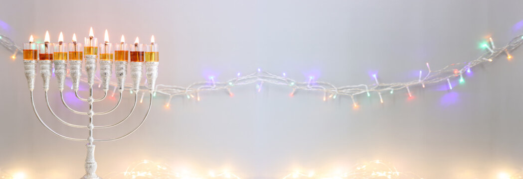 Image of jewish holiday Hanukkah with menorah (traditional candelabra) and oil candles over garland glitter lights background