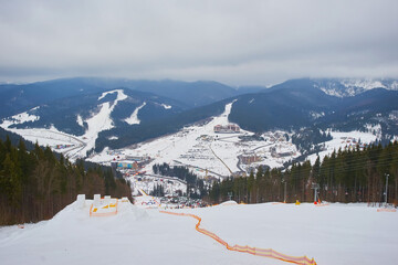 Fototapeta premium Ski resort in beautiful sunset light. View from the top: ski tracks, pine tree forest and mountains in the background.