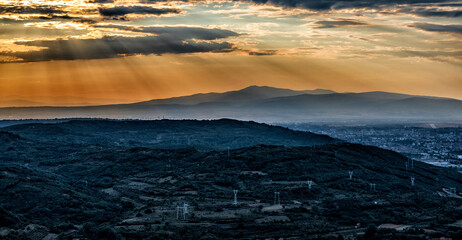 A landscape photo of a spectacular sunset over the mountain.
Orange sun rays breaking through the clouds, spreading the last glow over the mountain peaks, a small village at the base of the mountain