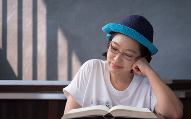Asian middle aged woman in casual style with eyeglasses reading textbook comfortably in vintage...