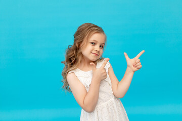 Happy cute little girl in a cotton white dress on a blue background in the studio laughing showing...