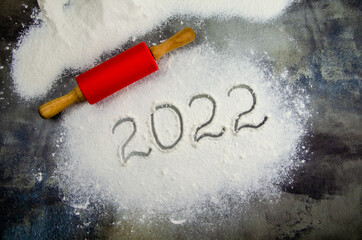 2022 sign is painted on flour. inscription 2022 is made of flour on black concrete background. Top view, flat lay, space for text. rolling pin, flour and numbers 2022. Christmas culinary background