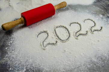 2022 sign is painted on flour. inscription 2022 is made of flour on black concrete background. Top view, flat lay, space for text. rolling pin, flour and numbers 2022. Christmas culinary background