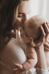 Beautiful young mother holds newborn baby girl in white lighter room at home. Tenderness cozy...
