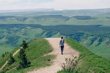 Obraz premium Lonely man walks along a mountain road into the distance.