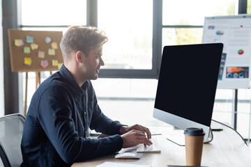 Side view of programmer using computer near coffee to go in office