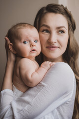 Beautiful young mother holds newborn baby girl in white lighter room at home. Tenderness cozy atmosphere