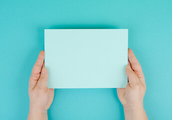 Fototapeta premium Woman holds a blank sheet of paper, blue colored background, empty copy space for text, minimalism
