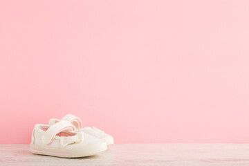 Fototapeta na wymiar White strap sandals with ribbon for little girl on table at light pink wall background. Pastel color. Closeup. Empty place for text. Front view.