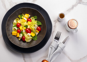 .Tropical salad containing iceberg lettuce, mint, mango, leek and cherry tomatoes on a white marble background.