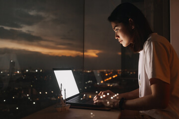 Asian woman work with laptop by the windows apartment with evening city view.