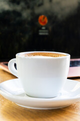 White big cup of cappuccino with foam on table. Morning coffee concept with stylish toning and place for text. A cup of coffee on the table near the laptop. Online classes, training, and blogging 