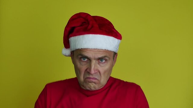 The man in the yellow background gestures with his hands and shakes his head. A man wearing a Santa hat and a red T-shirt on a yellow background is surprised and waving his hands.