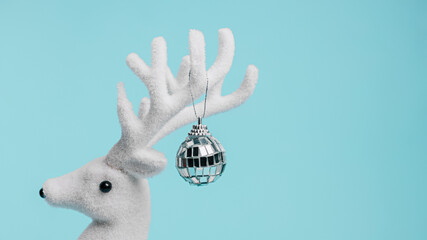 White reindeer with shiny disco ball hanging from antlers isolated on pastel blue background. Creative Christmas and New Year celebration party concept. Minimal holiday banner with copy space.