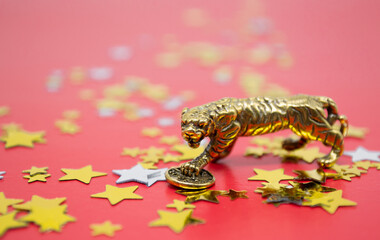 A bronze figure of a tiger with coin - symbol of the Chinese new year 2022 on a red background, gold and silver stars copy space. Wishes of good luck, financial well-being and wealth