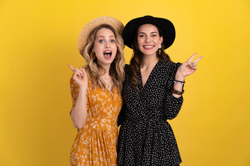 beautiful women friends together isolated on yellow background in black and yellow dress and hat