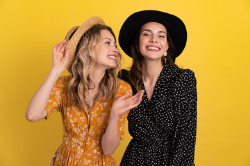 beautiful women friends together isolated on yellow background in black and yellow dress and hat