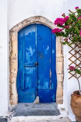 Greek island Kythira Chora, Greece. Blue wooden door and red bougainvillea on whitewashed wall.
