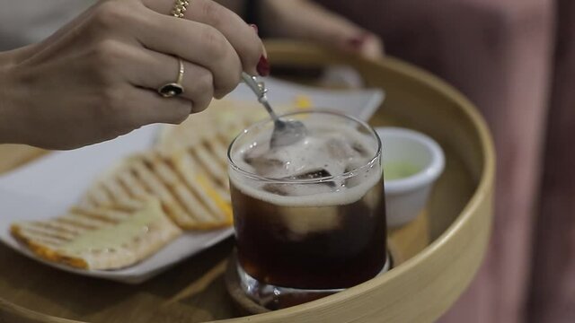 Joven bate con cuchara de metal a un te helado en vaso de cristal