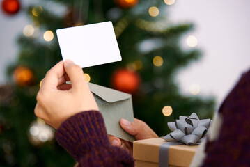 Hand holding mockup christmas greeting card and gift box for invitation design on christmas tree...