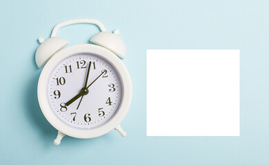 On a light blue background there is a white alarm clock and a white sheet of paper with a place to insert text or an illustration. Mockup