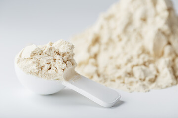 A mountain of soy protein isolate in powder with a measuring spoon on a white background.