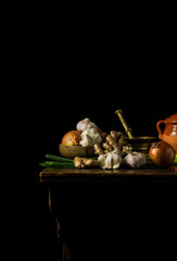 Still life of dried chilis, garlic, ginger spring onion and onion on wooden table against black background