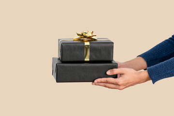 Hand holding black gift box on flesh color background.