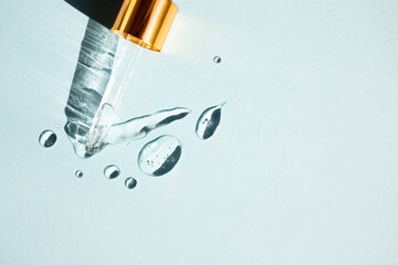 Drops of gel-like cosmetic liquid and a glass pipette on a blue background. Top view, place for...