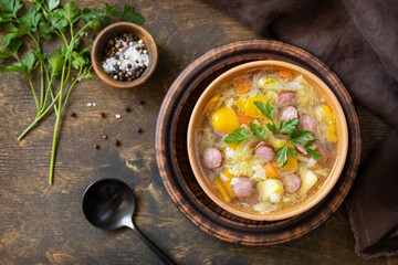 Czech food: Traditional Zelnacka cabbage soup with sausages and vegetables in a bowl on rustic wooden table. Top view flat lay background.