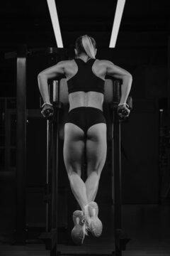A photo from behind of a woman who is doing push-ups on the uneven bars in a gym