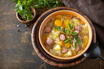 Czech food: Traditional Zelnacka cabbage soup with sausages and vegetables in a bowl on rustic wooden table. Copy space.