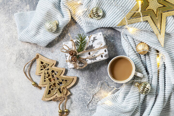 New Year's or Christmas composition. Cup of coffee, christmas star, knitted blanket, garland and gift on a gray background. Winter concept. Flat lay, top view.