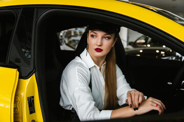 A young girl in a cap sits in a yellow car, taxi