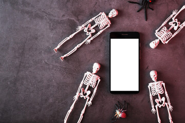Four skeletons are lying near the smartphone on a dark background.
