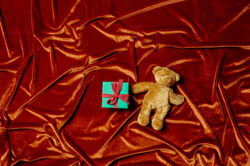 Holiday gift box with teddy bear toy on Crimson Red color fabric background.