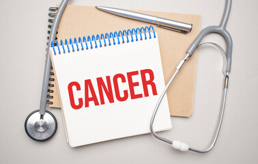 White notepad with the words cancer and a stethoscope on a blue background. Medical concept