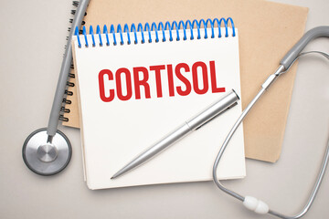 White notepad with the word cortisol and a stethoscope on a blue background. Medical concept