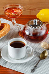 A teapot and a cup of strong aromatic tea on the table next to ginger and lemon ldem and donuts.