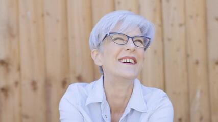 Slow motion portrait of an attractive happy mature senior woman laughing on wood background