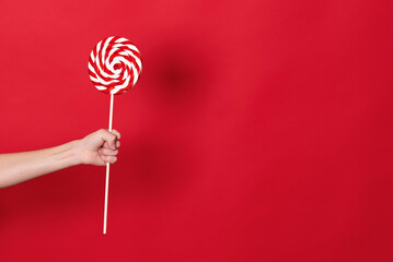 child's hand holding lollipop on red background 