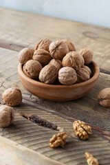 Dry Walnuts lie in a wooden bowl and several nuts are chopped on a wooden table. Rustic style. Healthy nutrition concept. Vertical orientation.