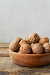 Young walnuts lie in a wooden bowl on a wooden table. Rustic style. Healthy nutrition concept. Vertical orientation. Copy space.
