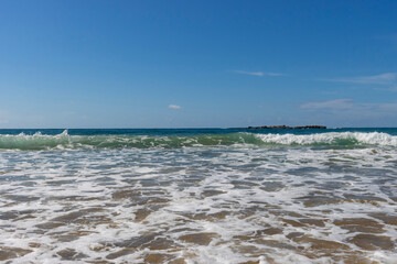 Foaming turquoise wave rolls over the sandy beach